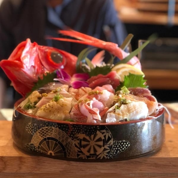 A decorative bowl of sushi and sashimi, garnished with a red fish head and orchids.