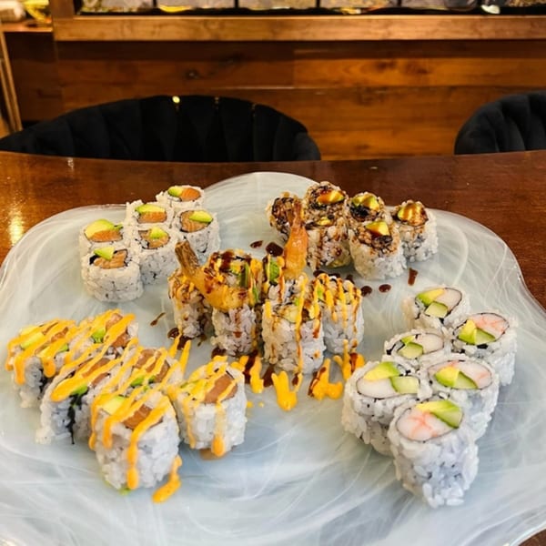 A large platter of various sushi rolls, including salmon, shrimp tempura, and crab, with sauces.