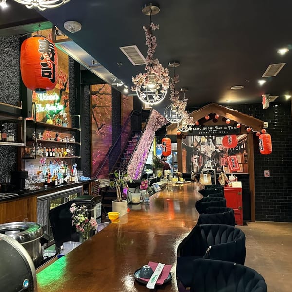Akeno Sushi Bar and Thai interior with a long bar, black chairs, and cherry blossom decor.