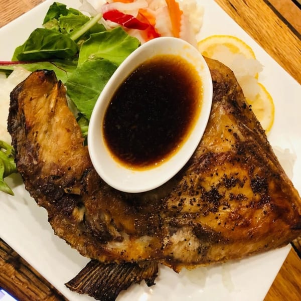 Grilled fish with a side of salad, lemon slices, and a small bowl of dark sauce.