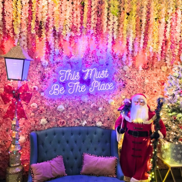 A festive Christmas display with a Santa Claus figure, blue couch, and neon sign.