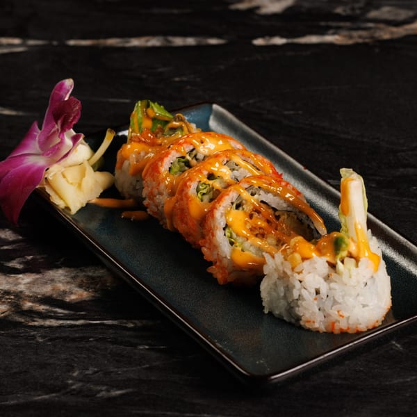 Akeno Sushi Bar and Thai's sushi roll with orange sauce, garnished with a purple orchid and ginger.
