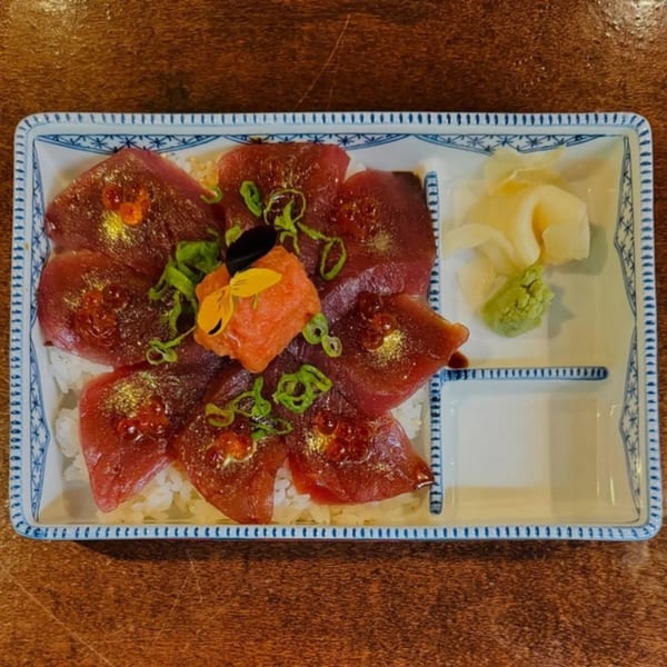 Akeno Sushi Bar and Thai's tuna sashimi over rice, garnished with roe, scallions, and edible flowers.