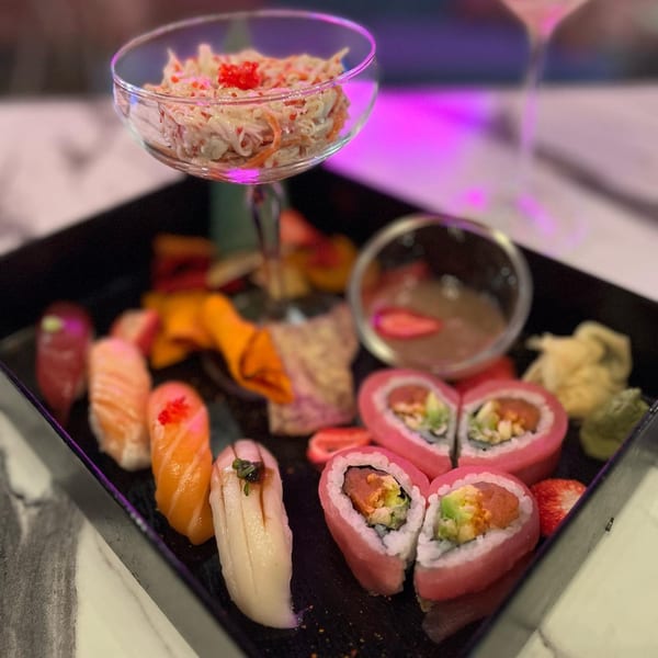 A sushi platter with various nigiri, heart-shaped pink rolls, and a crab salad cocktail.