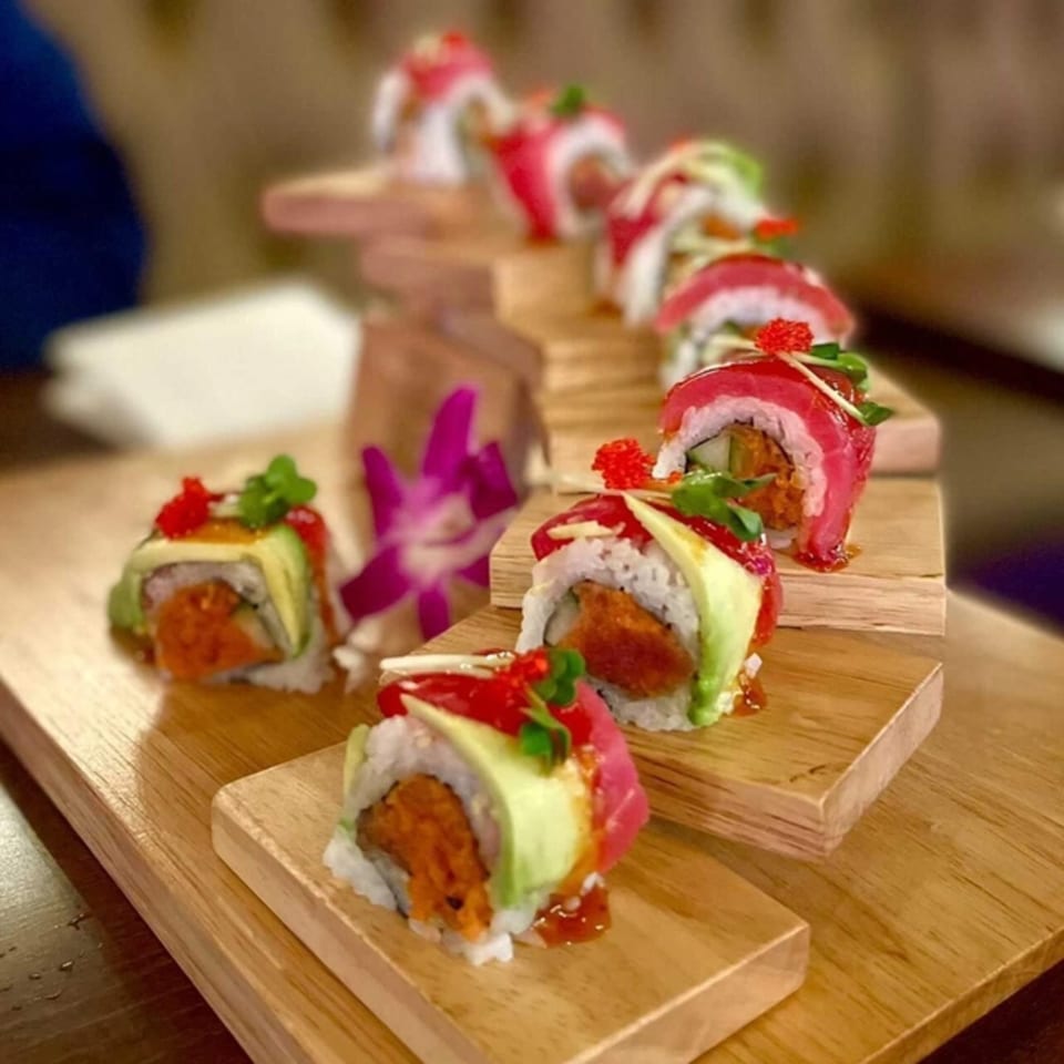 Akeno Sushi Bar and Thai's sushi rolls with tuna, avocado, and spicy sauce on a tiered wooden serving board.