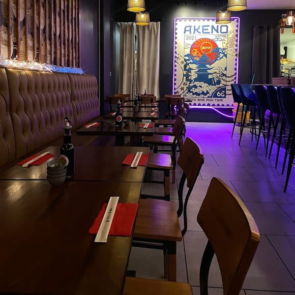 Interior of Akeno Sushi Bar and Thai, with dark wood tables, brown booth seating, and a neon sign.
