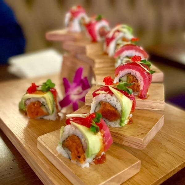 Akeno Sushi Bar and Thai's sushi rolls with tuna, avocado, and spicy sauce on a wooden tiered serving board.