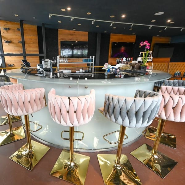 A modern bar area with a white circular counter and pink and gray velvet bar stools with gold bases.