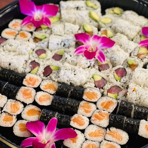 A large platter of various sushi rolls, including salmon, tuna, and avocado, garnished with pink orchids.