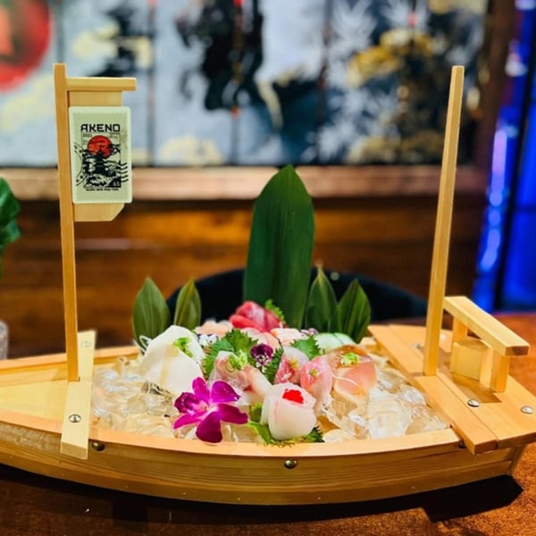 Akeno Sushi Bar and Thai's sushi and sashimi boat with various fish, garnishes, and an orchid.