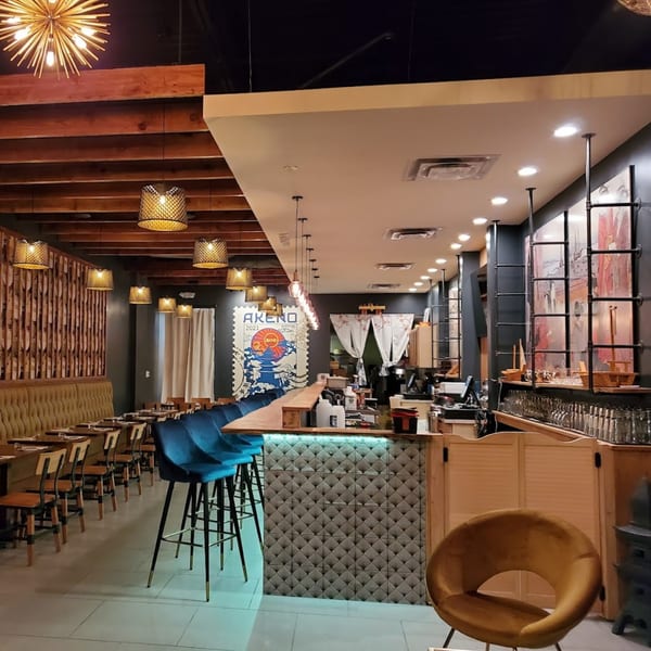 Interior of Akeno Sushi Bar and Thai, showing dining tables, a sushi bar with blue stools, and decorative lighting.